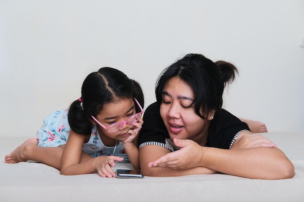 Une mère asiatique explique quelque chose à sa fille en regardant un film à l'aide d'un téléphone portable