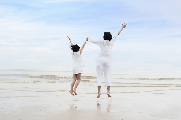 Mère asiatique avec fille tenant par la main, s&#39;amuser et sauter sur la plage.