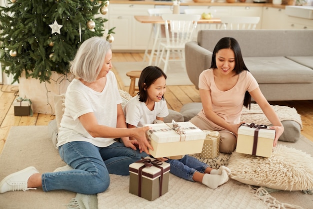 Mère asiatique avec ses deux filles assis sur le sol près de l'arbre de Noël et l'ouverture des cadeaux dans la chambre