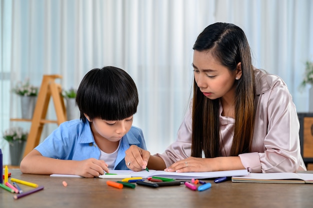 Une mère asiatique travaille à la maison avec son fils. Image de dessin de maman et d'enfant et art de peinture de couleur. Mode de vie de la femme et activité familiale.