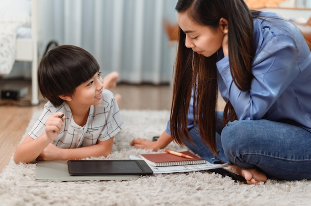 Une mère asiatique travaille à la maison avec son fils. Maman enseigne à un enfant pour l'apprentissage en ligne. Nouveau mode de vie normal et activité familiale.