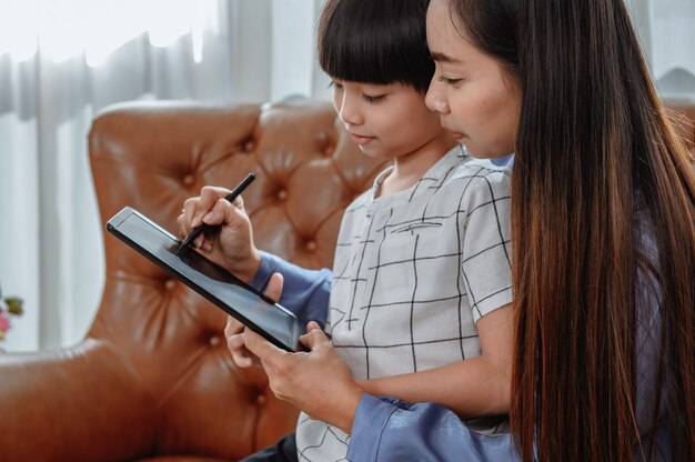 Une mère asiatique travaille à la maison avec son fils. Maman enseigne à un enfant pour l'apprentissage en ligne. Nouveau mode de vie normal et activité familiale.