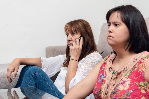 mère assise sur le sol du salon parlant au téléphone pendant que sa fille regarde la télévision