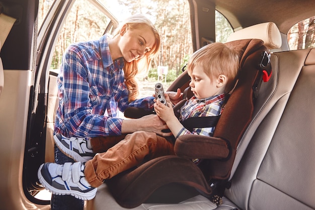 Mère attachant son petit garçon assis dans une voiture dans une chaise de sécurité route familiale