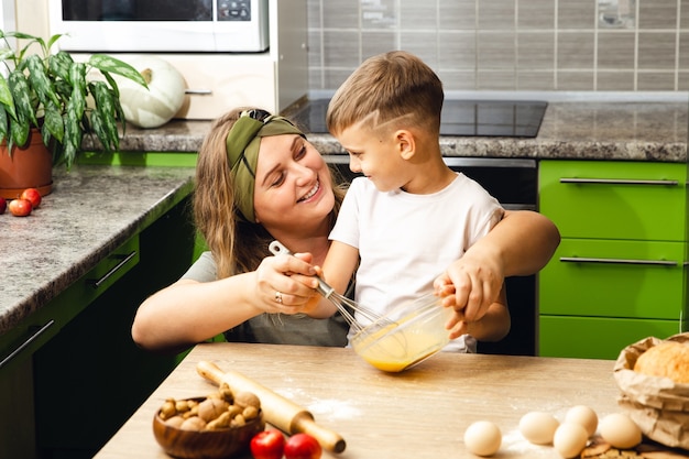 Mère attentionnée aide petit fils d'âge préscolaire à préparer des biscuits, souriant maman aimante apprendre à cuisiner avec petit garçon enfant, faire le déjeuner le week-end dans la cuisine ensemble