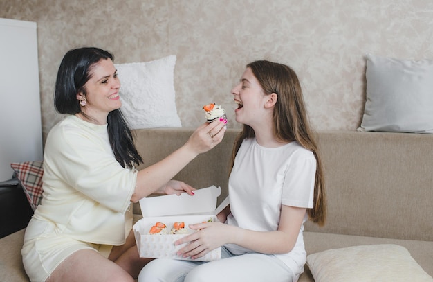 Une mère attentionnée et aimante donne à sa fille un délicieux gâteau assis sur le canapé