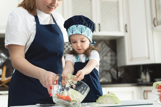 Mère attentionnée enseignant à sa petite fille à cuisiner une salade dans la cuisine