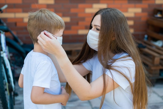 Une mère attentionnée met un masque sur son fils pour prévenir l'infection par le coronavirus Respect de la distance sociale et des normes sanitaires Femme et enfant à l'extérieur