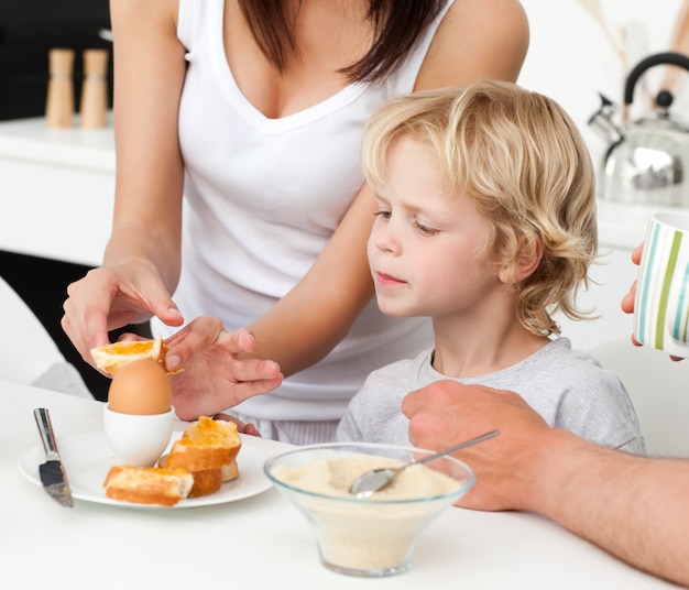 Photo mère attentive brisant un œuf à la coque pour son fils pendant le petit déjeuner