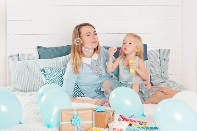 Mère attrayante et petite fille soufflant des bulles à la fête d'anniversaire à la maison