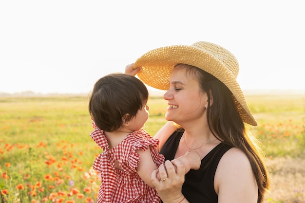 Mère au chapeau de paille avec sa fille enfant dans ses bras dans un champ de coquelicots au coucher du soleil