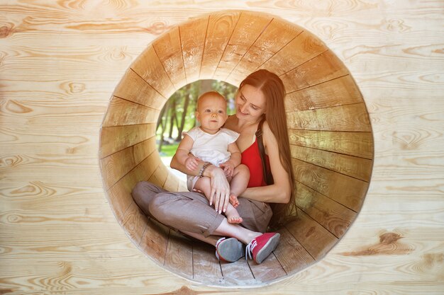 Mère et bébé assis dans un tunnel en bois. Aire de jeux écologique.