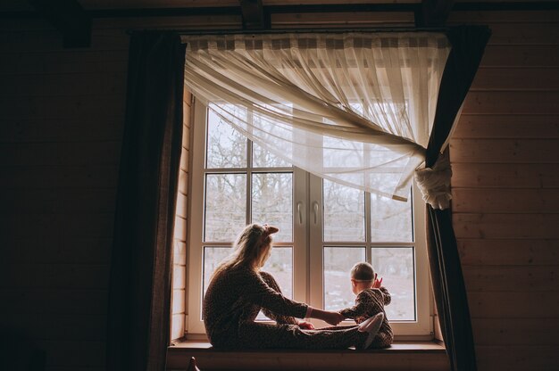 Mère avec bébé assis à la fenêtre et jouer