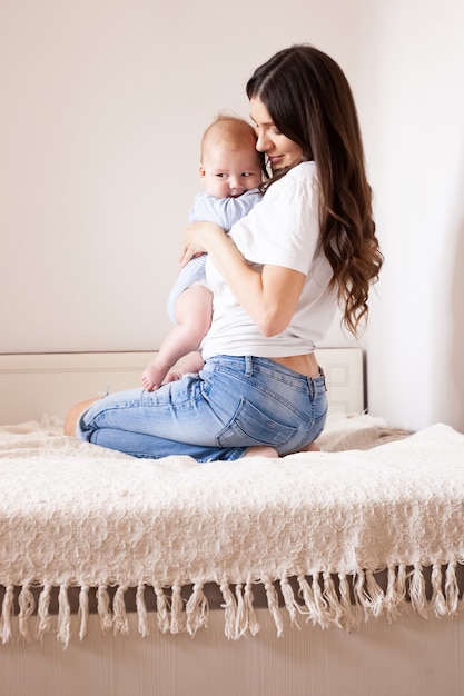 Mère et bébé au lit. Jeune maman jouant avec son fils nouveau-né. Enfant et parent ensemble à la maison. Famille avec enfants le matin. Femme de détente avec enfant dans une chambre ensoleillée. Bonheur et maternité