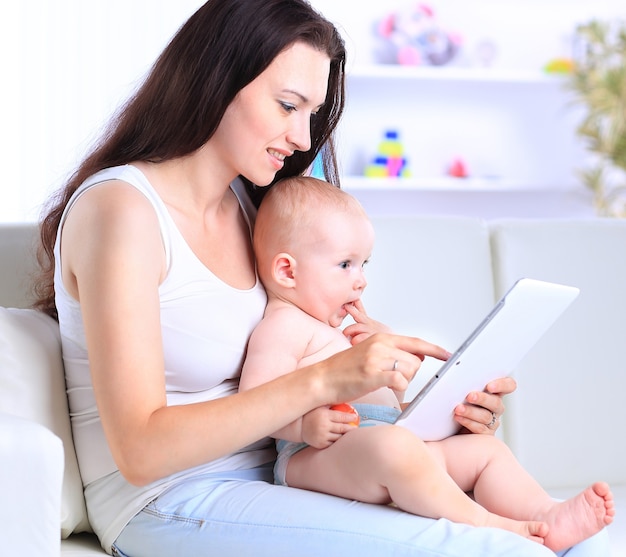 La mère et le bébé cherchent à jouer et à lire une tablette sur le canapé à la maison