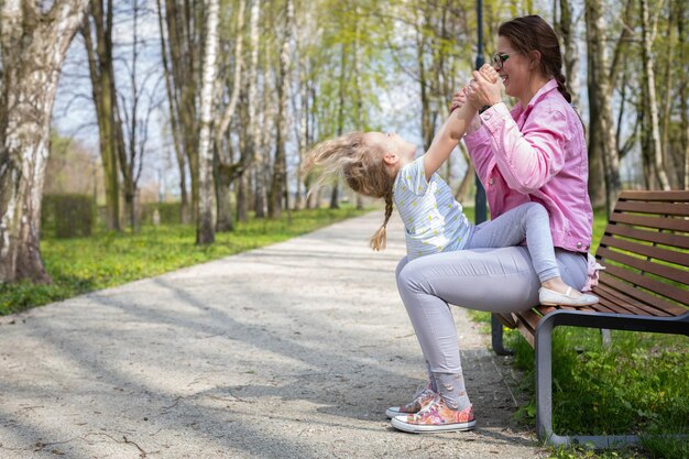 Une mère berce sa fille de haut en bas alors qu'elle est assise sur un banc dans un parc de la ville