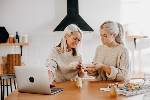 Mère blonde d'âge moyen et fille adolescente dans la cuisine regardant une recette ou une émission de télévision sur un ordinateur portable et un concept naturel de style de vie de cuisine