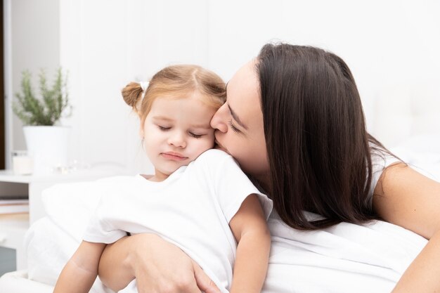 Mère brune adulte embrassant sa petite fille blonde