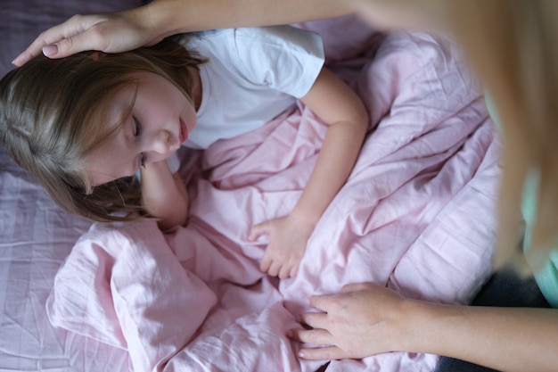 Mère caressant la tête de la petite fille triste au lit