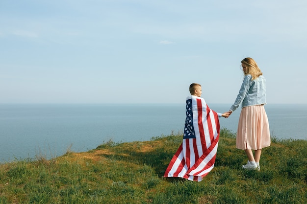 Mère célibataire avec fils le jour de l'indépendance des États-Unis. Femme et son enfant marchent avec le drapeau américain sur la côte de l'océan