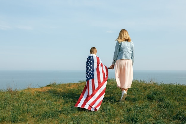 Mère célibataire avec fils le jour de l'indépendance des États-Unis. Femme et son enfant marchent avec le drapeau américain sur la côte de l'océan