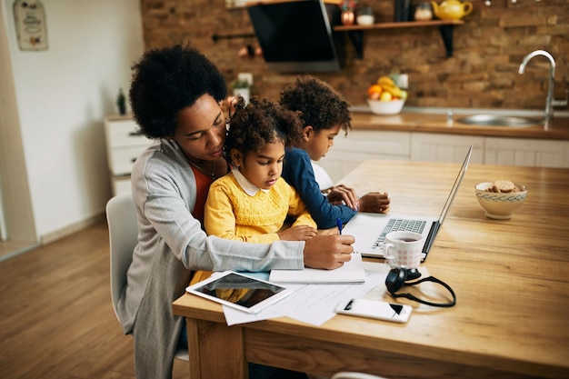 Mère célibataire noire prenant des notes et travaillant tout en gardant ses enfants à la maison