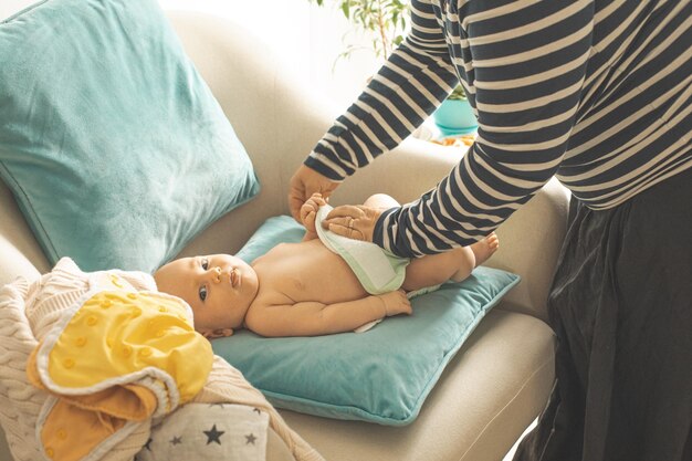 La mère change une couche réutilisable sur son nouveau-né sur la chaise