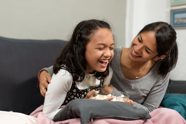 Mère chatouillant sa fille dans l'intimité de sa maison sur le canapé.