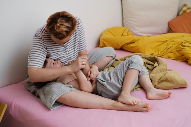 La mère chatouille l'enfant dans le lit qui joue le matin.