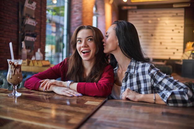 Mère chuchotant des commérages et racontant un secret à sa jeune fille surprise à l'oreille dans un café