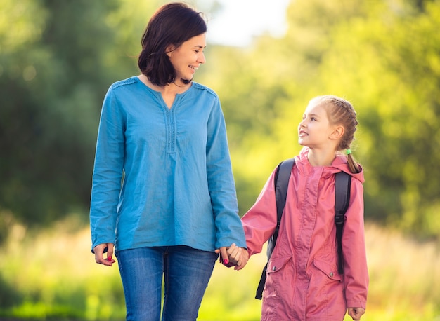 Mère conduisant sa fille à l'école sur la nature ensoleillée