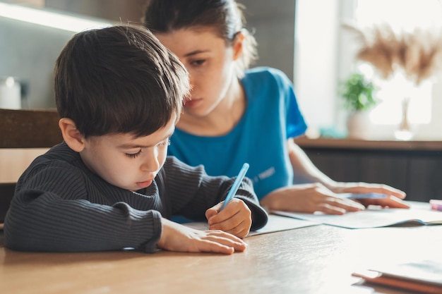 La Mère Contrôlant De Temps En Temps Son Fils Qui Fait Ses Devoirs Assis à La Même Table