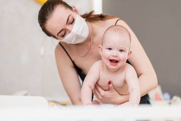 Une mère dans un masque de protection est assise à la maison avec un enfant en quarantaine pendant la pandémie de coronovirus et de covid-19.