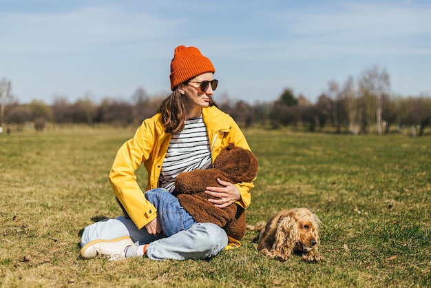 une mère dans une veste jaune est assise sur l'herbe dans le parc et allaite un bébé bambin dans sa main