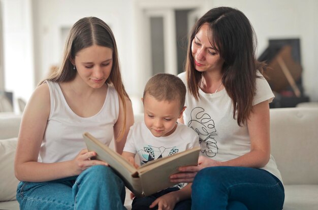 mère et deux enfants sur le canapé à la maison regardent un livre d'images