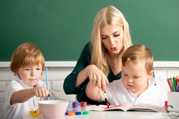 Mère et deux fils dessinent ensemble de la peinture maman aide les enfants garçons enseignant aide les écoliers à apprendre