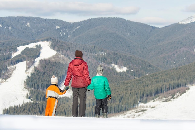 Mère et deux fils sont debout sur un fond de montagnes enneigées Vue arrière Journée ensoleillée d'hiver