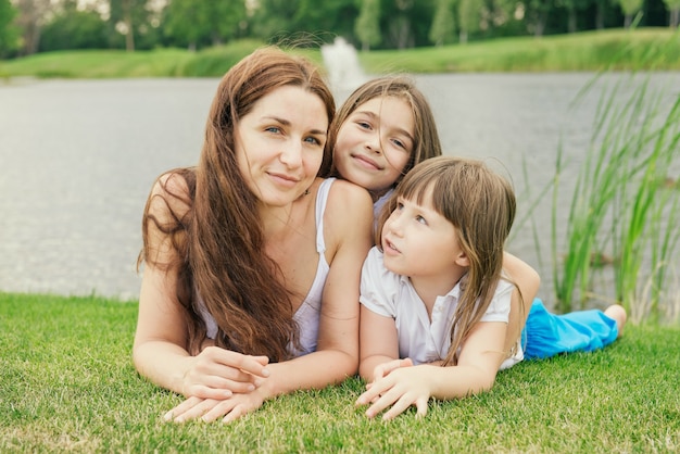 Mère avec deux jeunes filles se reposant sur l'herbe dans le parc près du lac