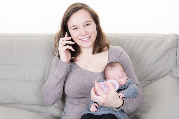 Mère donne le biberon à son nouveau-né tout en restaurant son téléphone portable sur le canapé du salon