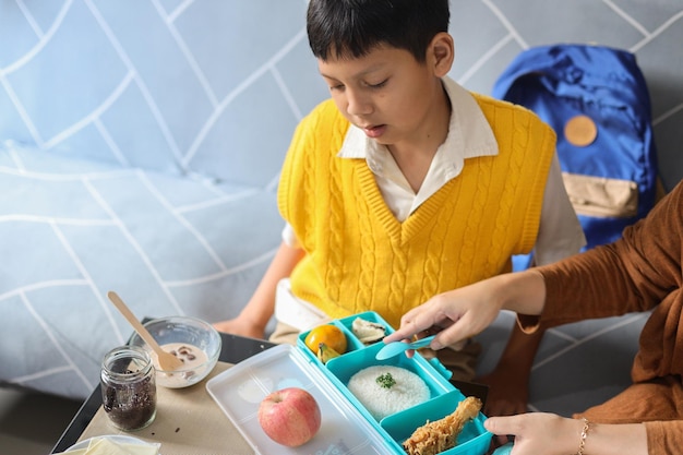 La mère donne un déjeuner savoureux dans une boîte à son fils pour qu'il se prépare à l'école.