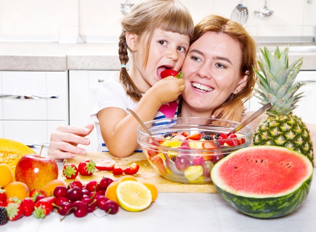 mère donne à la petite fille une salade de fruits dans la cuisine.