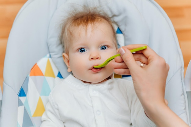 La mère donne de la sauce aux fruits à bébémaman nourrit bébé sur une chaise hautenourriture pour bébé