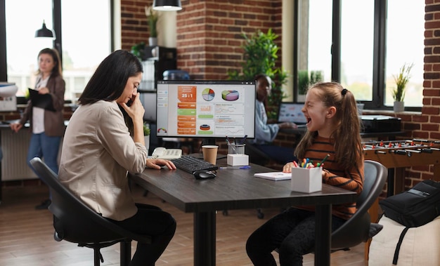 Une mère embarrassée et irritée assise à la table du travail pendant que sa fille ennuyeuse et bruyante crie. Jeune femme d'affaires gênée par une petite fille bruyante et irritante.