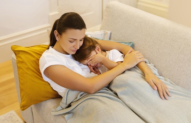 Mère embrassant enfant endormi pendant qu'ils se détendent sur le canapé confortable à la maison