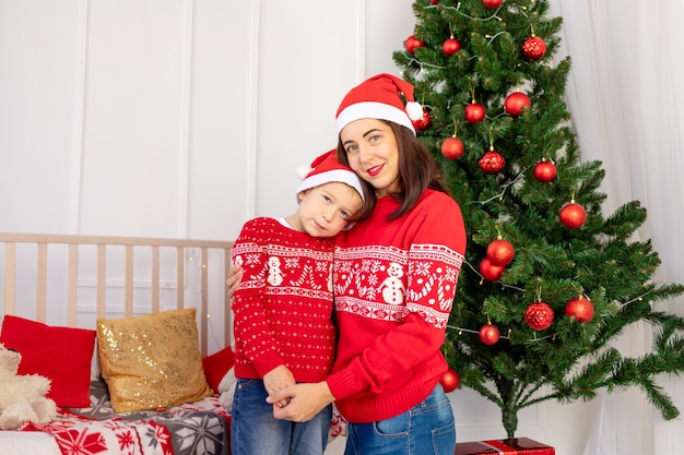 Mère embrasse un enfant en pulls rouges près de l'arbre de Noël