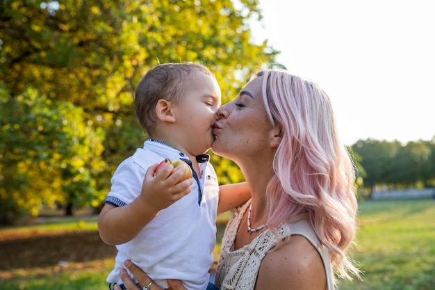 Mère embrasse tendrement son bébé sur la bouche lors d'une promenade dans le parc