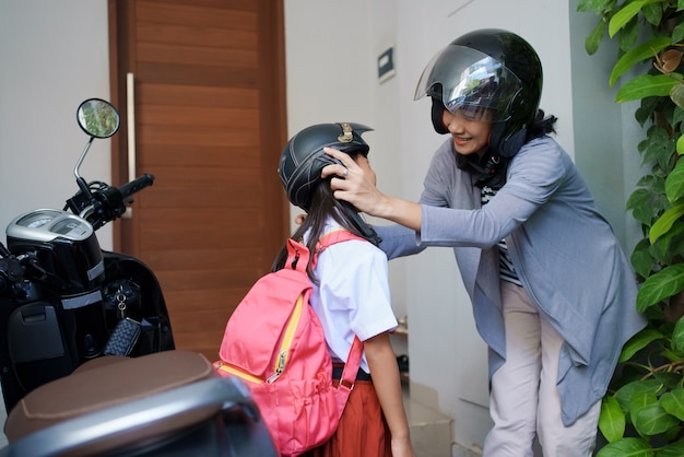 Mère emmenant sa fille à l'école en moto le matin. élève du primaire asiatique en uniforme retournant à l'école