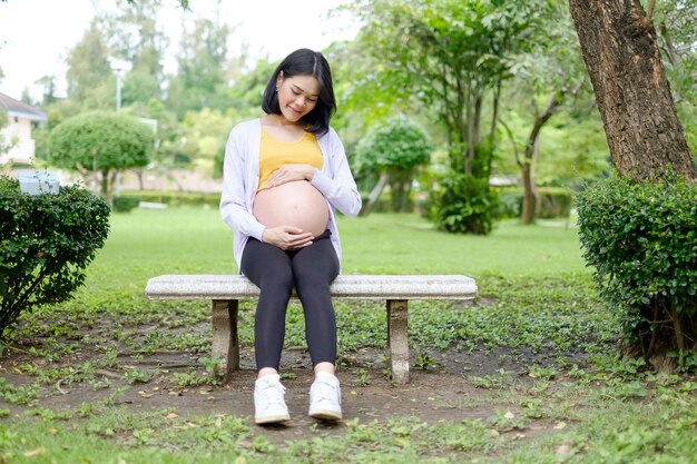 Une mère enceinte portant des vêtements décontractés jaune-violet est assise dans le jardin.