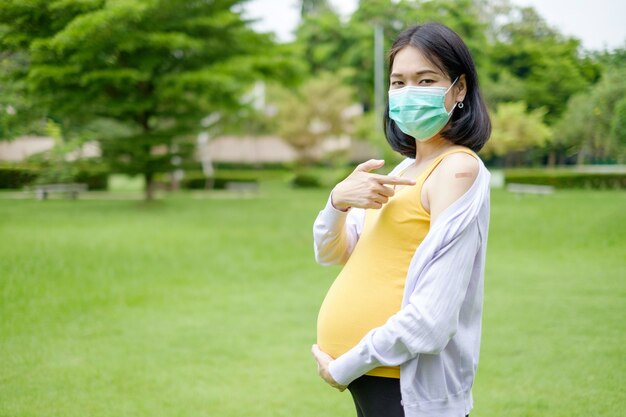 Une mère enceinte portant des vêtements décontractés violets et jaunes montre du plâtre sur le haut de son bras