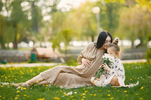 Mère enceinte et sa petite fille assise sur une herbe dans un parc